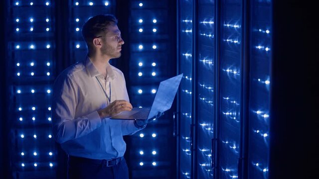 Male Server Engineer in Data Center. IT engineer inspecting a secure server cabinet using modern technology laptop coworking in data center.