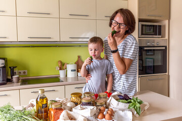 Adult woman and her son are eating a fresh cucumber. Vegetarian food. Communication of a mother with a child at home
