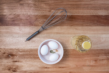 wooden worktop with a whisk, 3 chicken eggs, a bottle of oil and a container to prepare homemade mayonnaise. Free text space