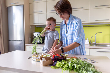 Boy child helps his mom to cook vegetable ratatouille standing in the kitchen. Family traditions.