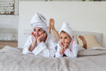 Mom and daughter are dressed in white terry robes, lie on the bed. Nursing communication in the family.