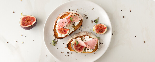 a plate of bruschettas with cream cheese, ham and figs on a light marble table
