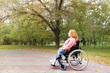 disabled teenage girl on a wheelchair for a walk in the autumn park smiling and looking into the...