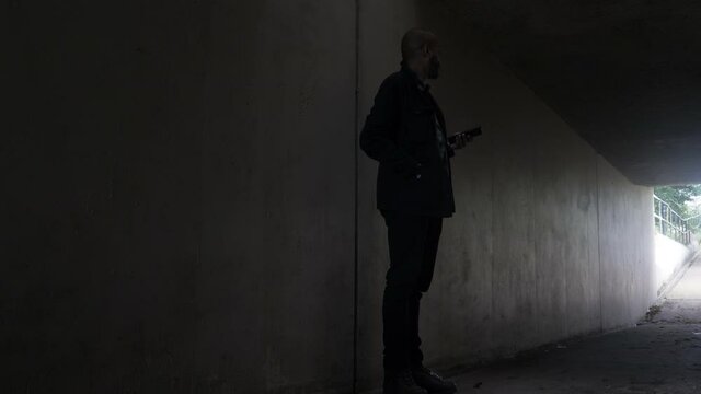 Shady Bald Ethnic Minority Checking Mobile Waiting In Underpass Tunnel, Looking Side To Side. Locked Off, Low Angle