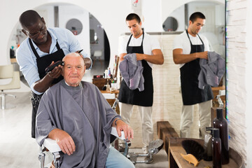Fototapeta premium Elderly man getting haircutting with electric clipper from professional African barber in salon