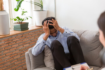 Obraz premium Young Asian man talking his problems with professional psychologist while conducting a consultation and making notes to seek advice and therapy
