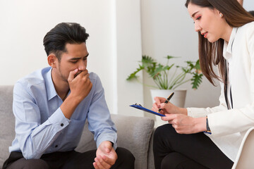 Young Asian man talking his problems with professional psychologist while conducting a consultation and making notes to seek advice and therapy