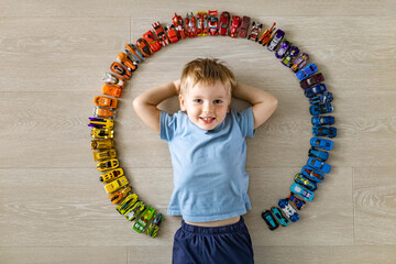 Laughing little cute baby boy lying in circle of car model toys hot wheels collection top view