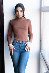 portrait of a young beautiful woman in blue jeans, stands near the window