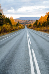 A long asphalt road going to the mountains, around the autumn forest and mountains. Travel with your family by car, relax in nature and fresh air.