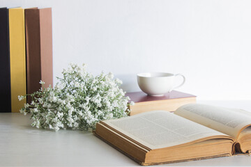 Book with flowers and coffee cup on table with nature light. 