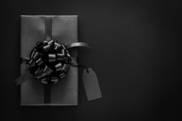 A black gift box with ribbon and blank price tag puts on black background. Black friday and Boxing day concept.