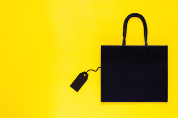 Black shopping paper bag with blank black price tag on yellow background for Black Friday shopping sale concept.