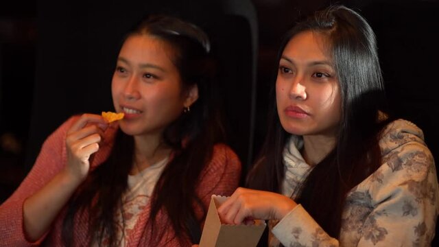 Friends in a cinema have fun while watching a movie and eating popcorn