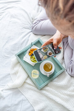 Young woman in having breakfast the morning while lying in bed. Girl takes pictures of her food for social networks.