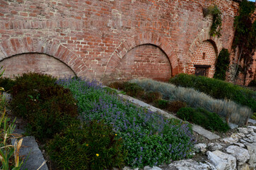 herb beds in rows above a limestone stone back, a brick walled courtyard with a gravel path in the park. monastic healing garden with a focus on the blind. the blind try scents and textures. 