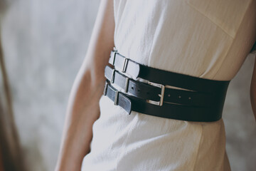 A slim girl in a white dress tries on a belt with black leather