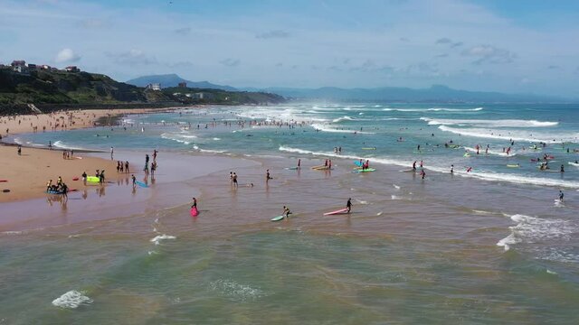 many surfers with boards go into the ocean on the coast of Biarritz.