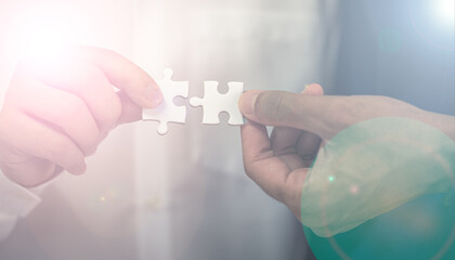 two hands of businessman to connect couple puzzle piece with sky background.Jigsaw alone wooden puzzle against sun rays.one part of whole.symbol of association and 
connection. business strategy