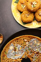 Rajasthani Ghevar. Ghewar is an Indian crunchy sweet dish made using refined flour, sugar, and ghee. Garnished with silver foil and dry fruits. Over dark background with copy space.