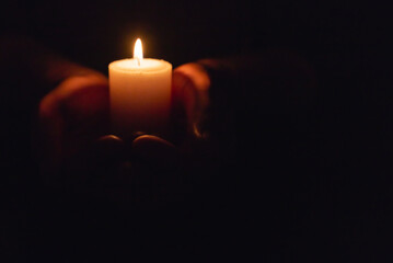 Hands holding burning candle in dark like a heart.Selective focus,black background.Copy space.