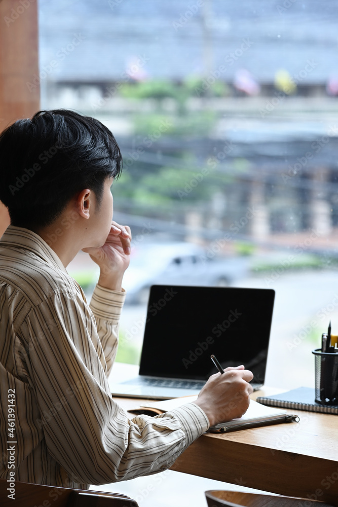 Poster side view man freelancer sitting near window and working with laptop computer.
