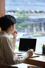 Side view man freelancer sitting near window and working with laptop computer.