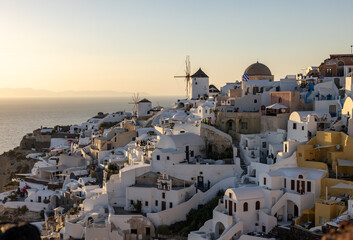 Fototapeta na wymiar Whitewashed houses and windmills in Oia in warm rays of sunset on Santorini island. Greece