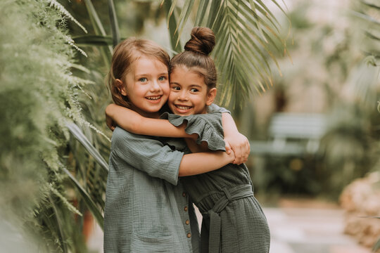 Portrait of two charming smiling girls belonging to different races surrounded by tropical leaves. Friendship, linen clothing, environmental friendliness. High quality photo
