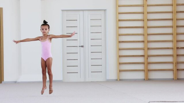 A little girl in swimming suit performing gymnastic exercise in pink ballet studio