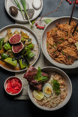 asian dinner with ramen soup, spicy noodle and cucumber salad top view on black background closeup. Selective focus