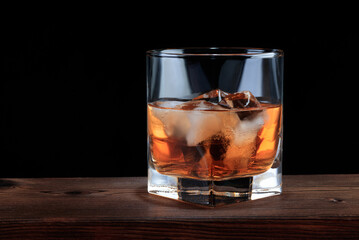 Glass of whiskey with ice on a wooden background. Soft focus.