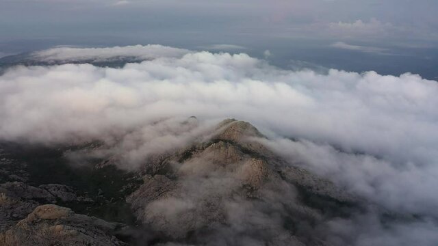 View from above, flying above the clouds, stunning aerial view of a granitic massif surrounded by moving clouds during a beautiful sunrise. Mount Limbara (Monte Limbara) Sardinia, Italy.	