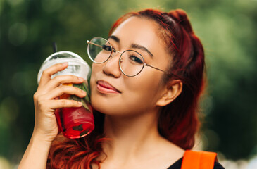 Fashionable portrait of Asian woman, with a backpack, hipster walking on the street, drinking a delicious cocktail
