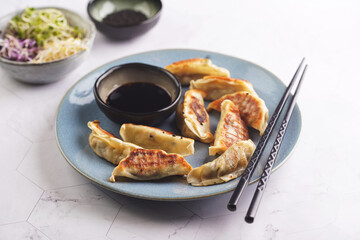 Japanese dumplings gyoza stuffed with chicken meat on a blue plate with soy sauce, microgreens, sesame seeds and black chop sticks