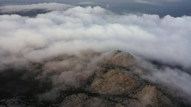 View from above, flying above the clouds, stunning aerial view of a granitic massif surrounded by moving clouds during a beautiful sunrise. Mount Limbara (Monte Limbara) Sardinia, Italy.	