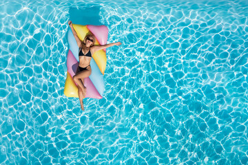 Aerial top down view of a beautiful woman in bikini on a colorful float enjoying the fresh swimming pool water during summer time