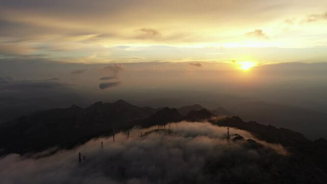 View from above, flying above the clouds, stunning aerial view of a mountain range with an antenna farm surrounded by clouds during a beautiful sunrise. Mount Limbara (Monte Limbara) Sardinia, Italy.