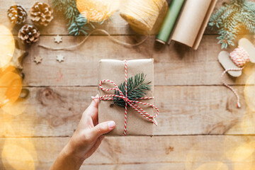 A hand holding Christmas gift box wrapped in kfaft paper with pine tree branch