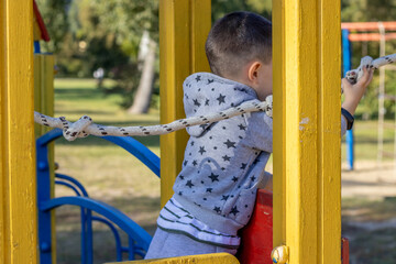 Fototapeta premium park,playground for kids,sunny summer day.kid is climbing and​ hanging​ from​ steel,iron, bars.iron rusted round rings,climbing rope ladder.slide, have fun, outdoor activities