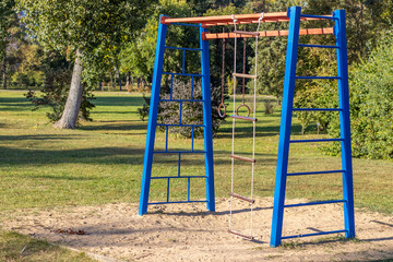 Fototapeta premium park,playground for kids,sunny summer day.kid is climbing and​ hanging​ from​ steel,iron, bars.iron rusted round rings,climbing rope ladder.slide, have fun, outdoor activities