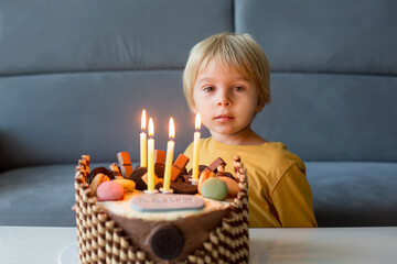 Cute child, boy, celebrating his birthday at home with colorful cake