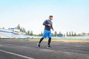 Muscular young man in headphones running at stadium