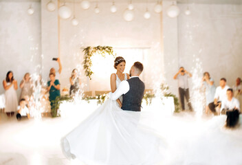 The first dance of the newlyweds in an elegant hall with guests and with the use of heavy smoke.