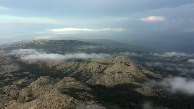 View from above, flying above the clouds, stunning aerial view of a granitic massif surrounded by moving clouds during a beautiful sunrise. Mount Limbara (Monte Limbara) Sardinia, Italy.	