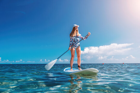 Healthy happy fit woman in bikini relaxing on a sup surfboard, floating on the clear turquoise sea water. Recreational Sports. Stand Up Paddle boarding. Summer fun, holidays travel. Active lifestyle