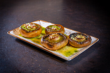 Mushrooms with olive oil and garlic on a black background, on a white plate