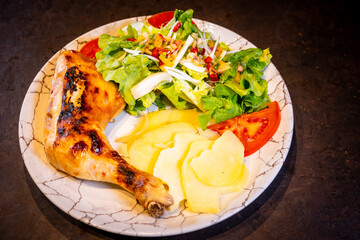 Salad with chicken thigh and salad on a black background, on a white plate