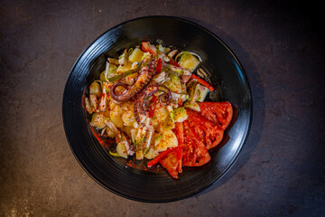 Salad with potatoes and octopus with spicy paprika on a black background, on a black plate