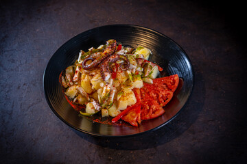 Salad with potatoes and octopus with spicy paprika on a black background, on a black plate